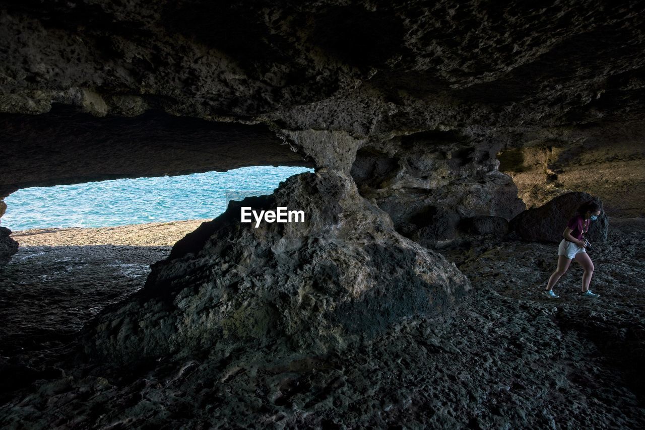 Young woman walks through a natural cave next to the sea