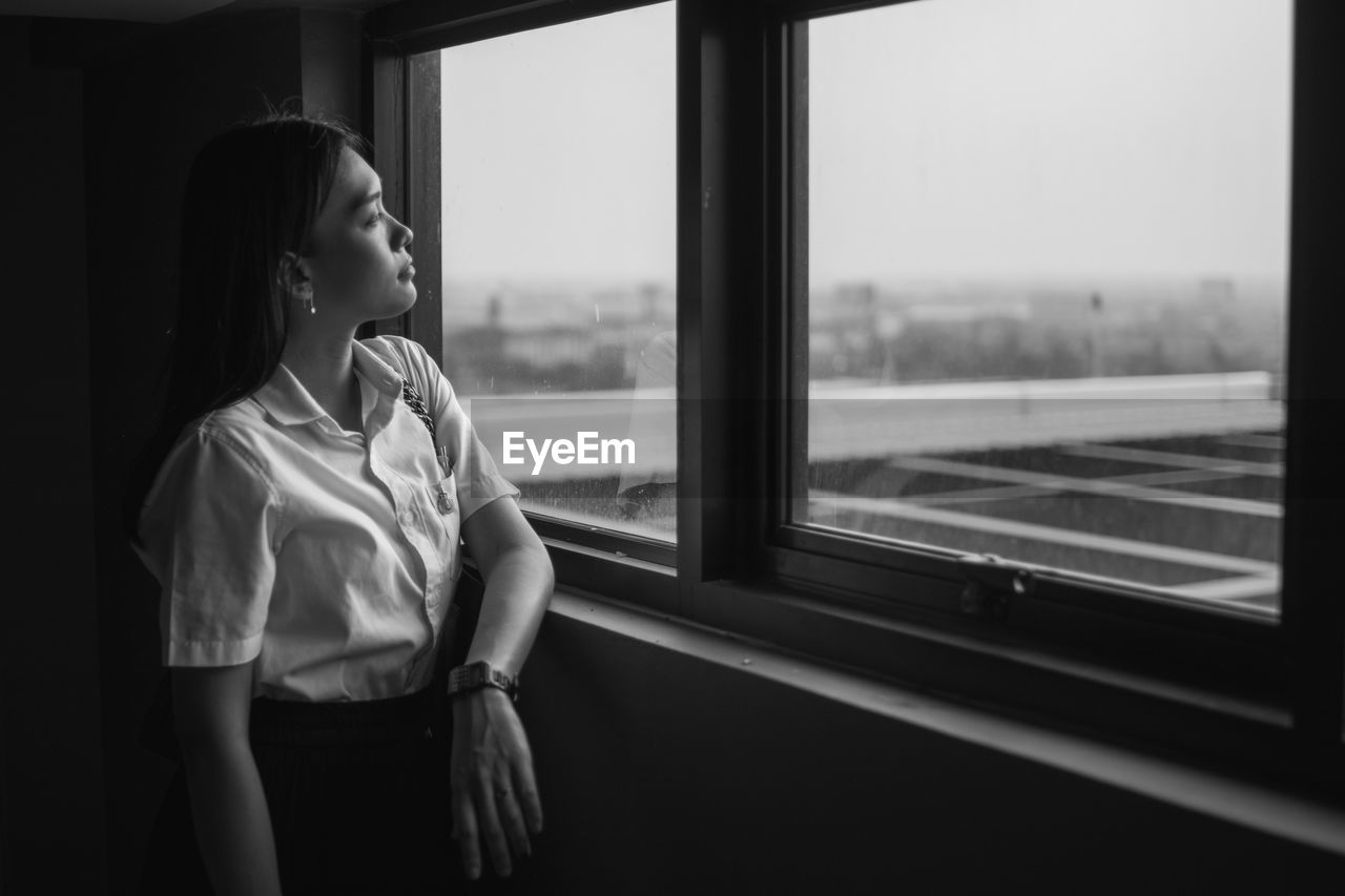 Young woman looking through window at home