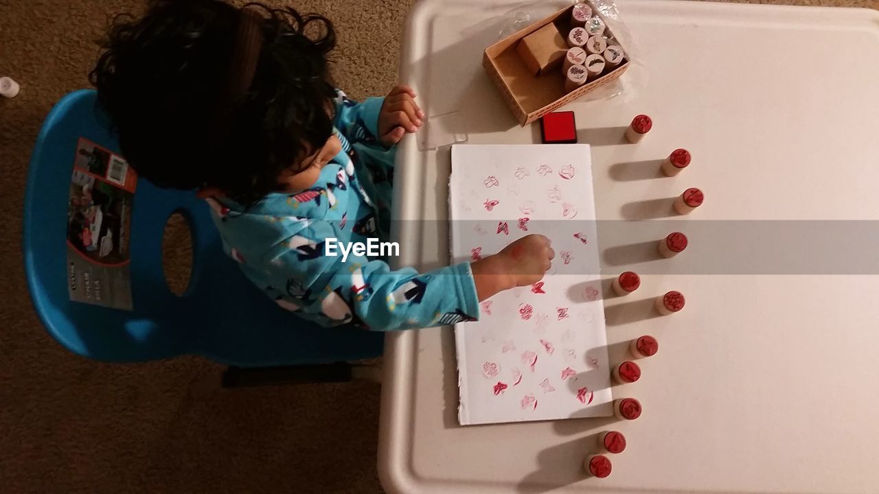 High angle view of little girl painting with stamps on table