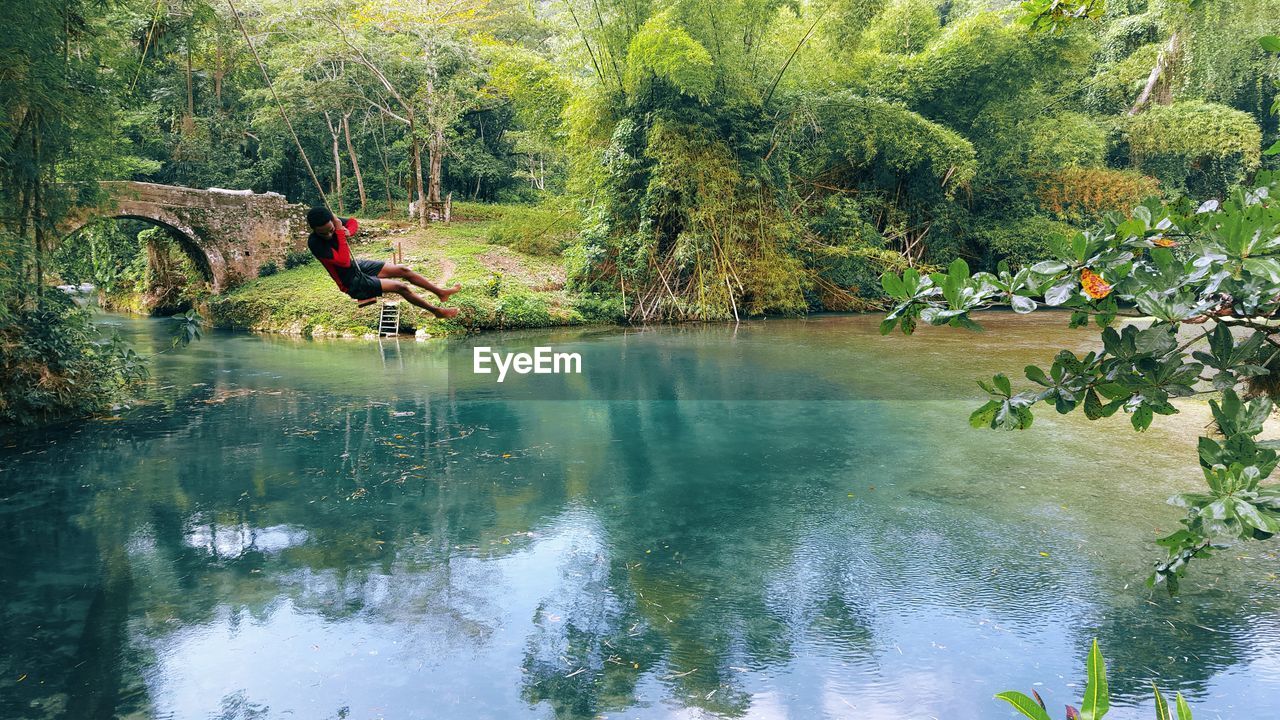 Man swinging above calm river