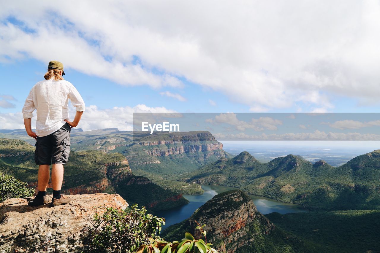 Rear view of man standing on rock while looking at valley against sky