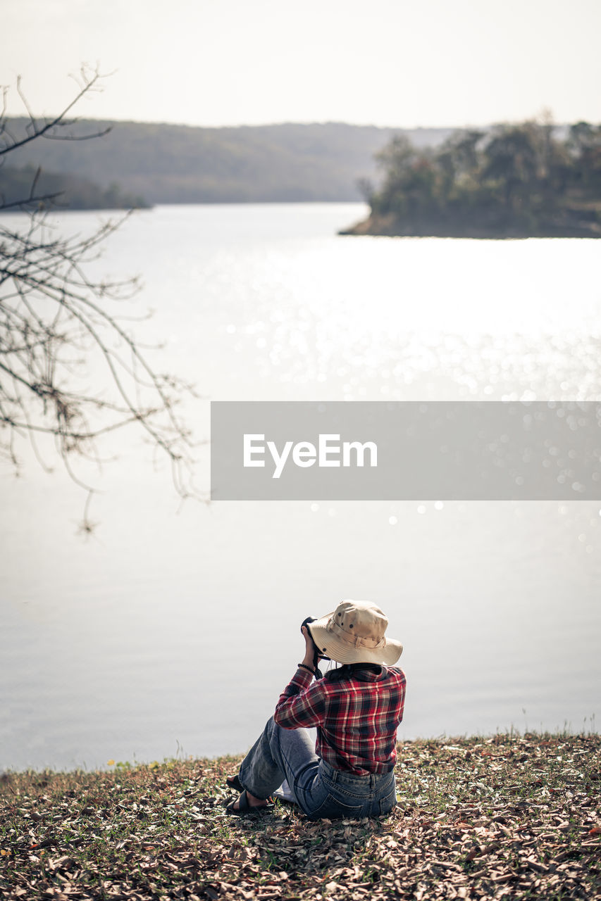 rear view of woman sitting by lake against sky