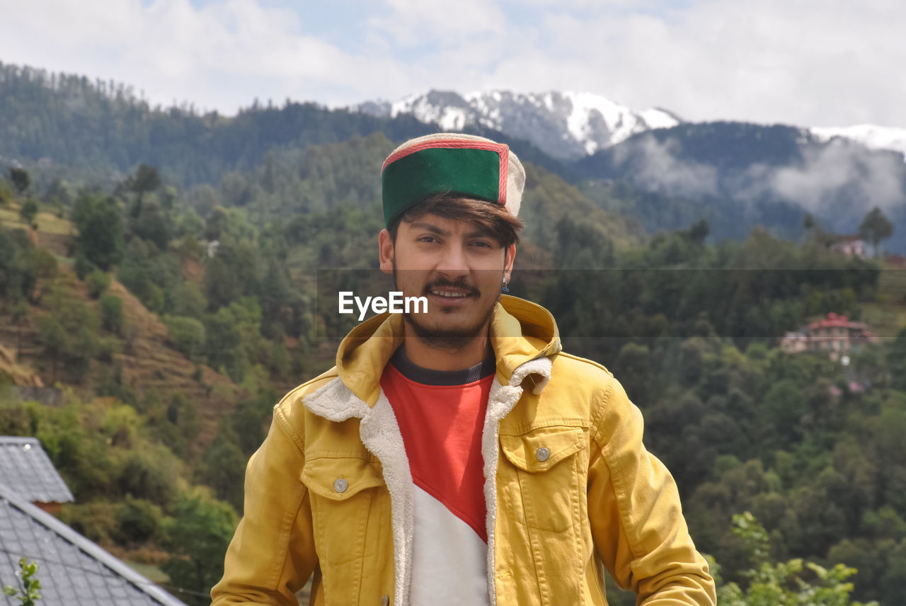 A north indian young men standing outdoor against beautiful mountains.