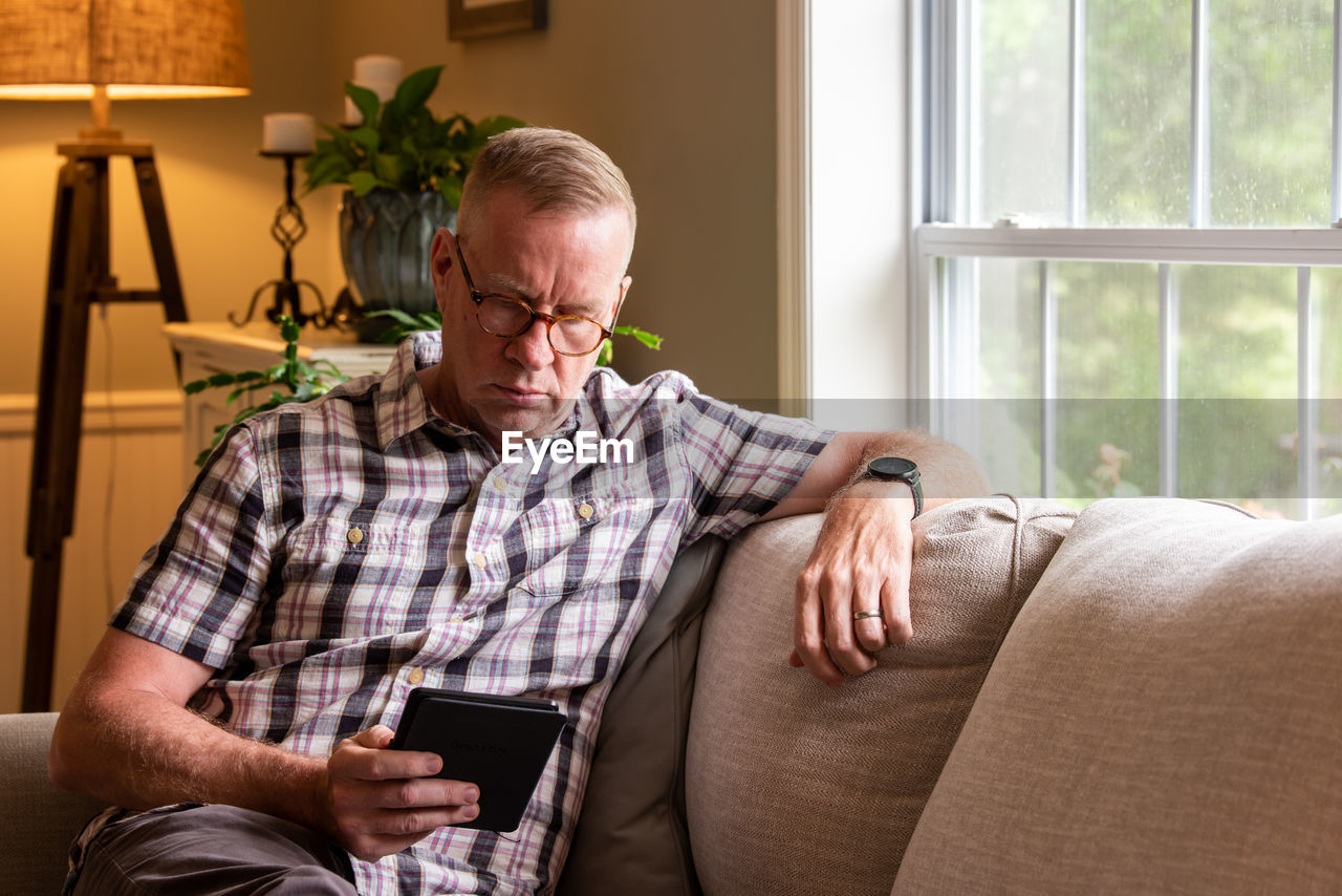 Senior man looking at digital tablet sitting on sofa at home