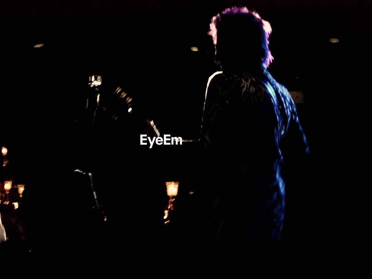 REAR VIEW OF WOMAN STANDING IN ILLUMINATED DARK