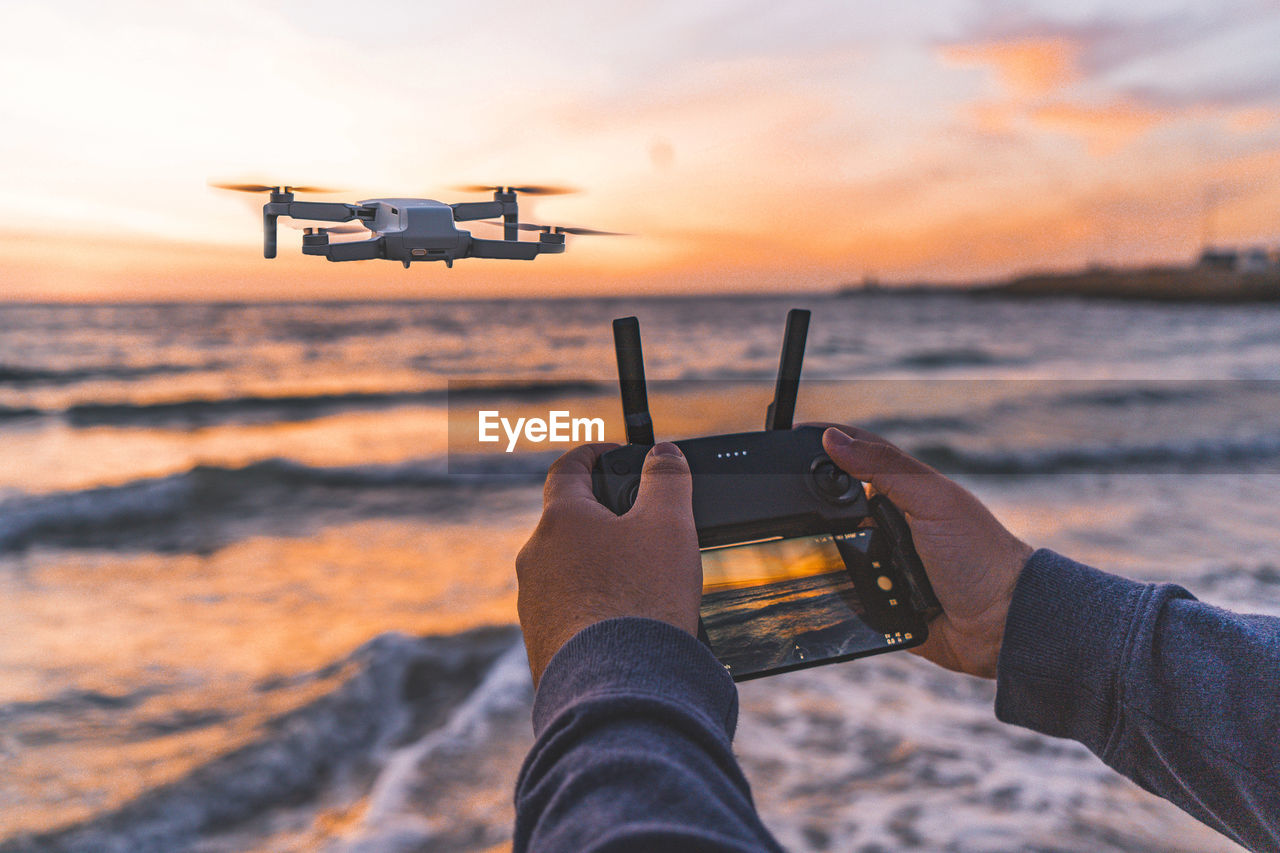 Cropped hands of person operating drone with remote control on beach