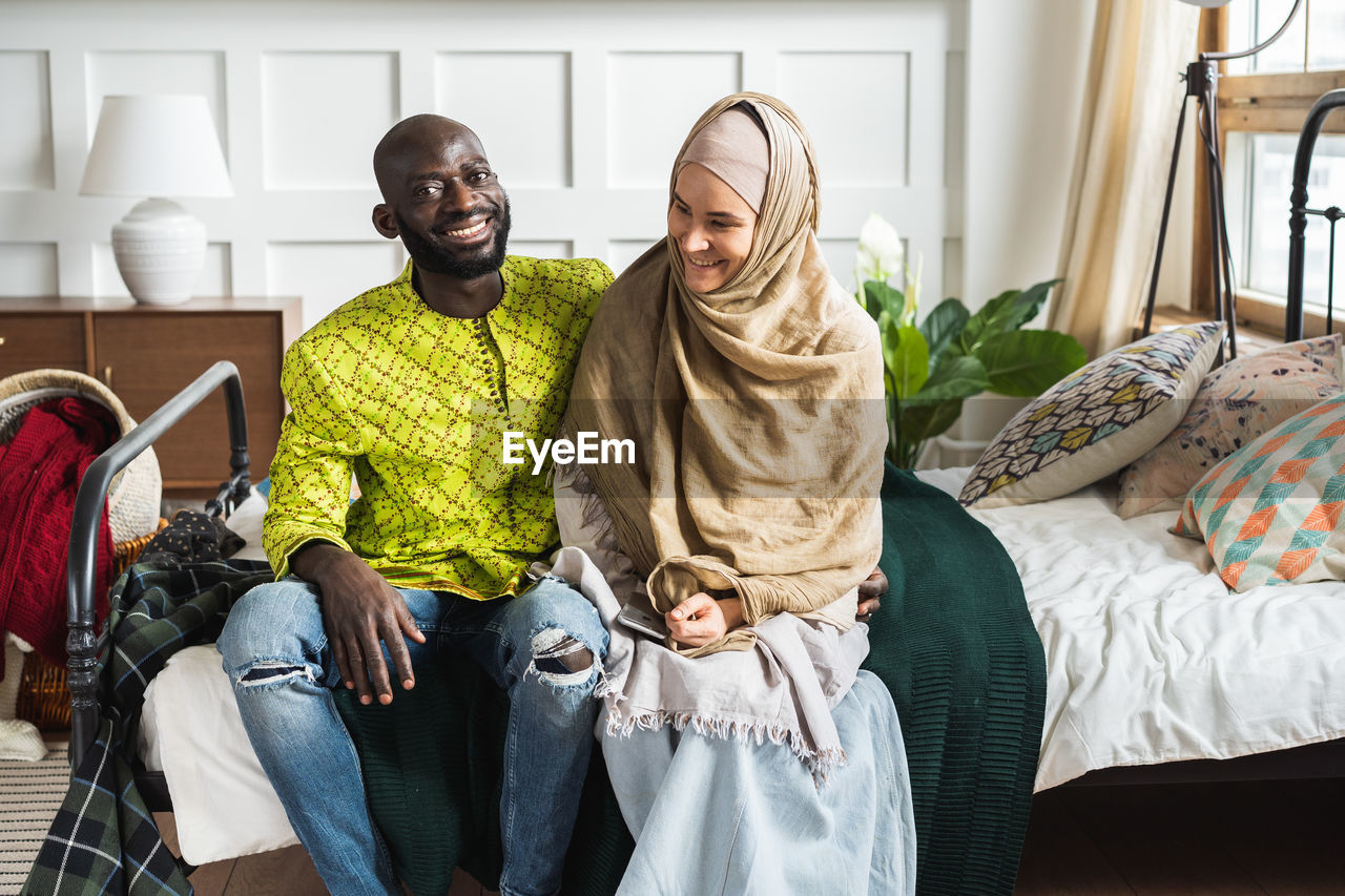 Smiling couple sitting on bed at home