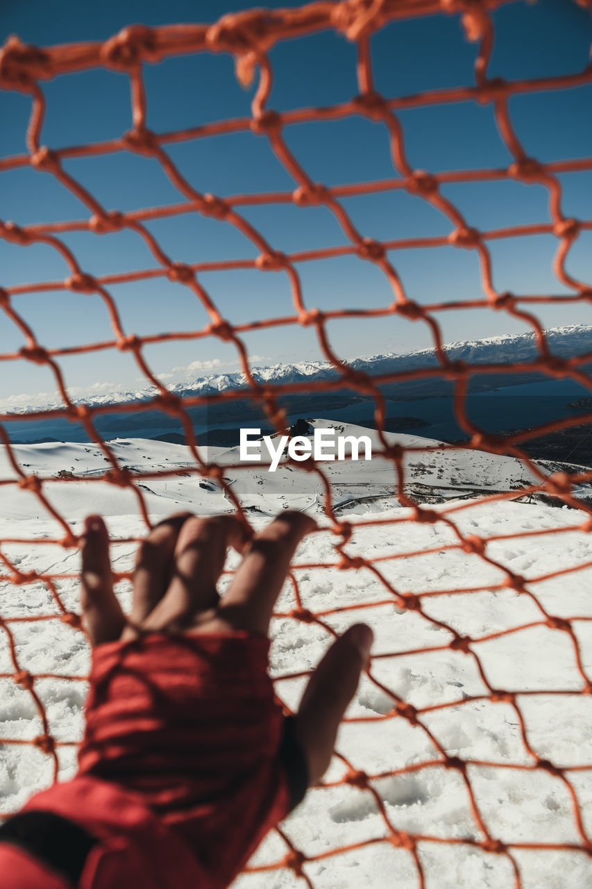 Cropped hand of woman holding net against sky during winter