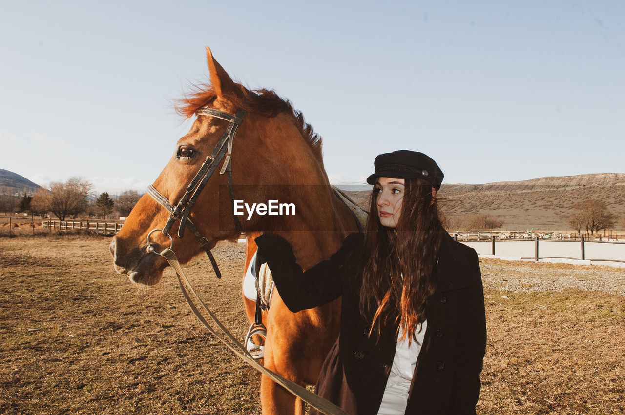 Young woman looking away while standing with horse in animal pen