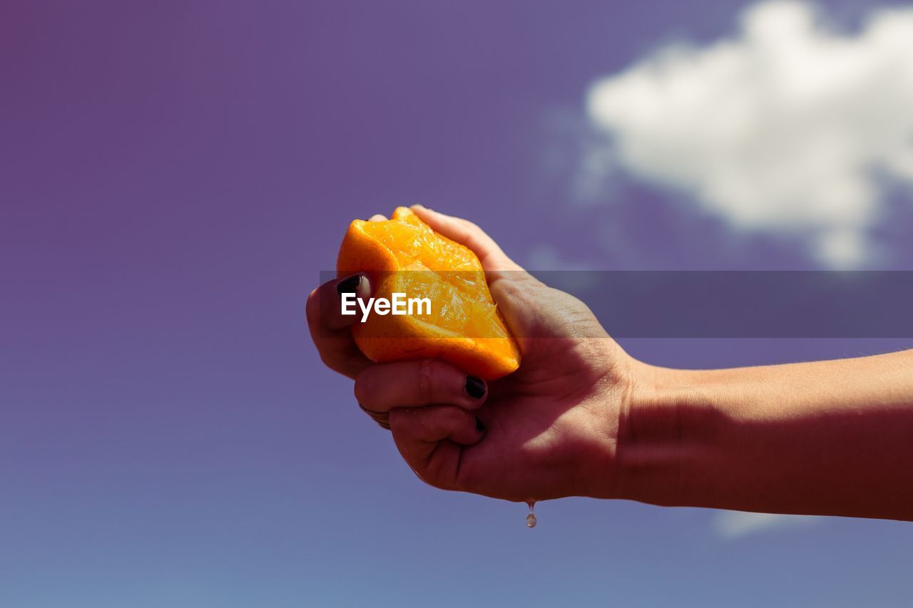 Close up of person holding orange against sky