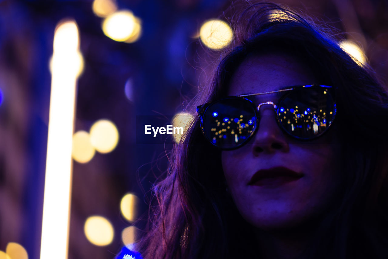 Close-up of woman wearing sunglasses outdoors at night