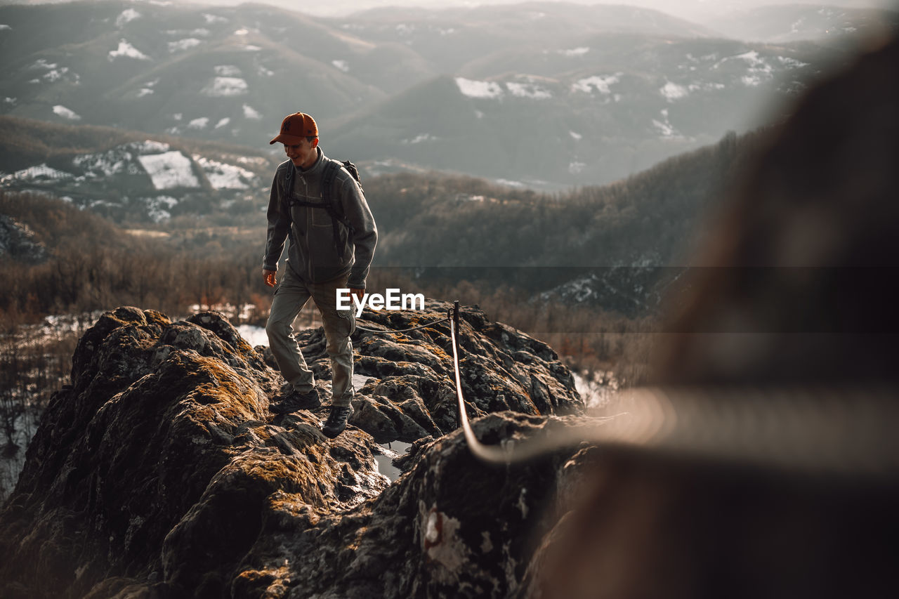 REAR VIEW OF MAN STANDING AT MOUNTAIN