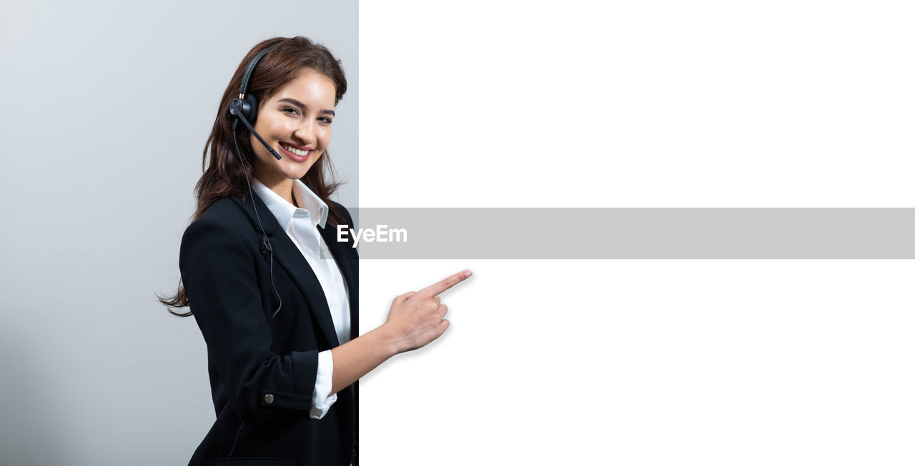 PORTRAIT OF A SMILING YOUNG WOMAN STANDING ON WALL