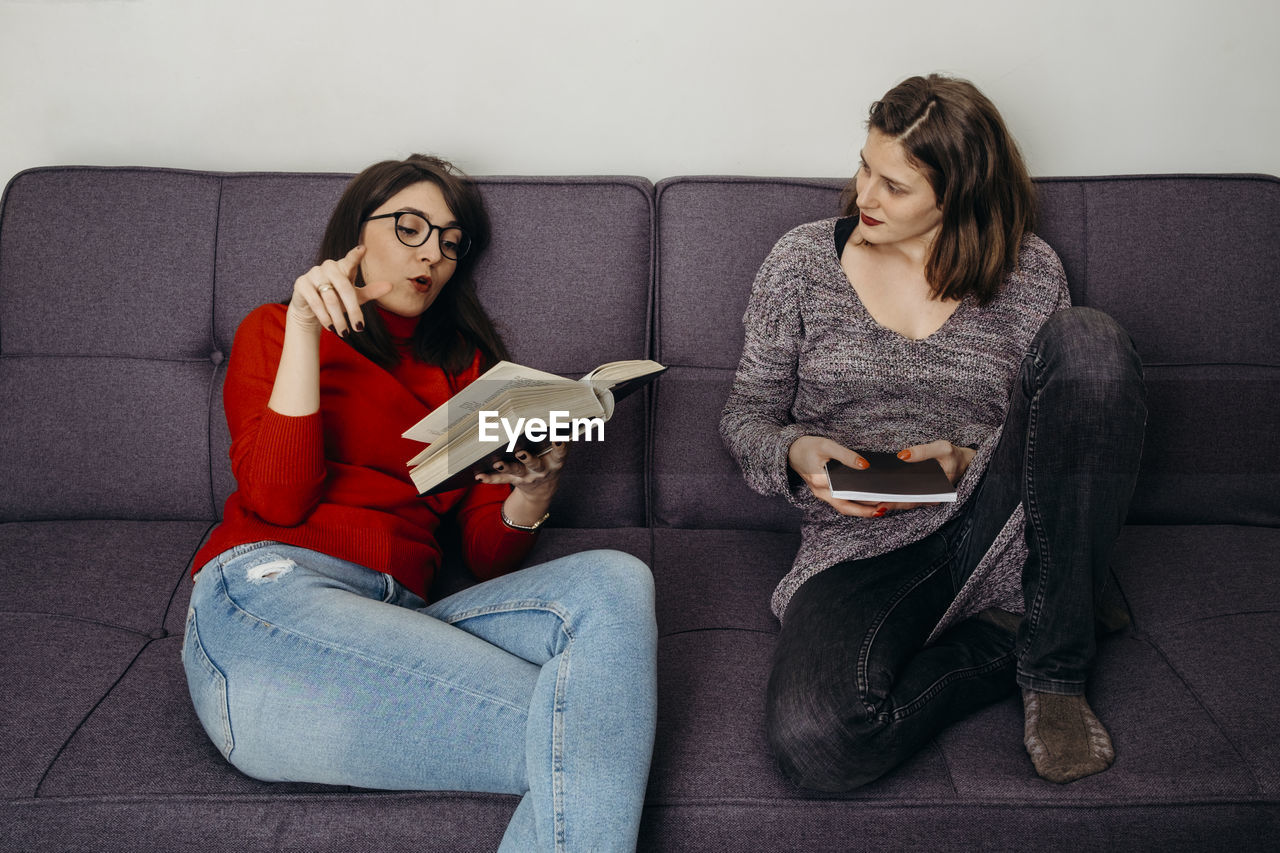 Young females holding book sitting on sofa at home