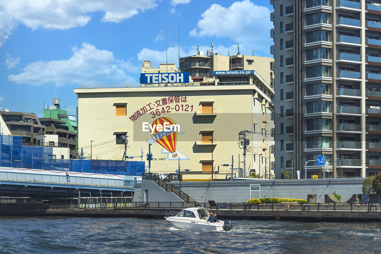 SAILBOATS ON RIVER BY BUILDINGS AGAINST SKY