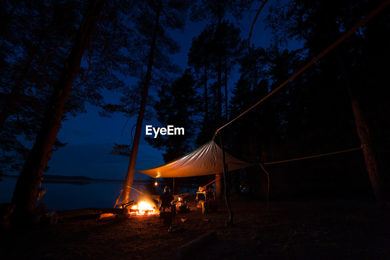 VIEW OF TENT ON FIELD AGAINST TREES AT NIGHT