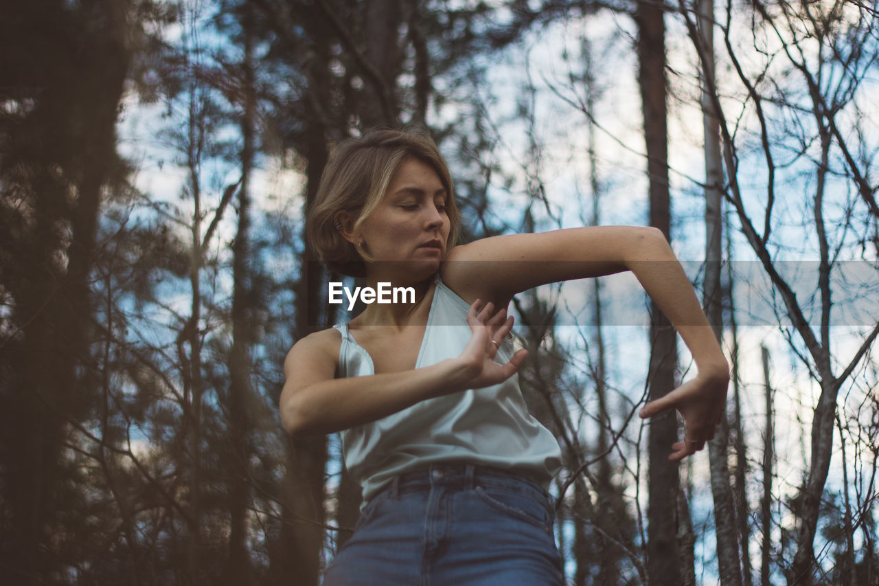 Low angle view of young woman dancing in forest