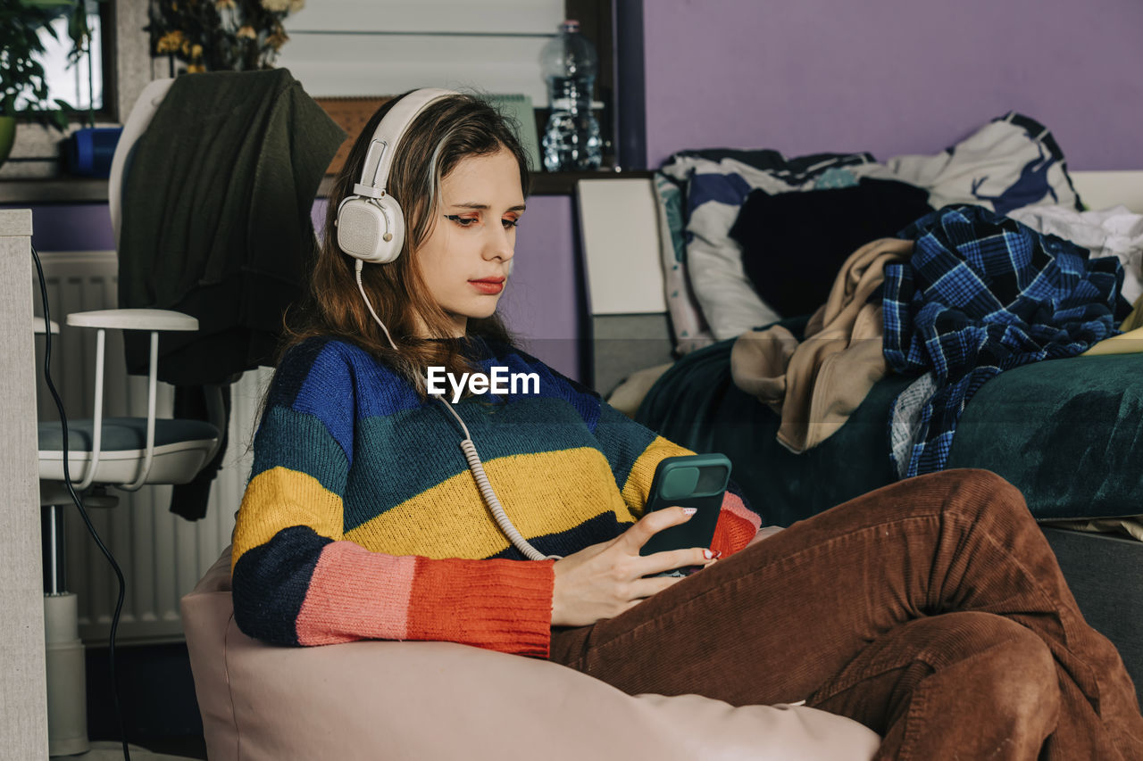 Girl using smart phone listening to music through headphones at home