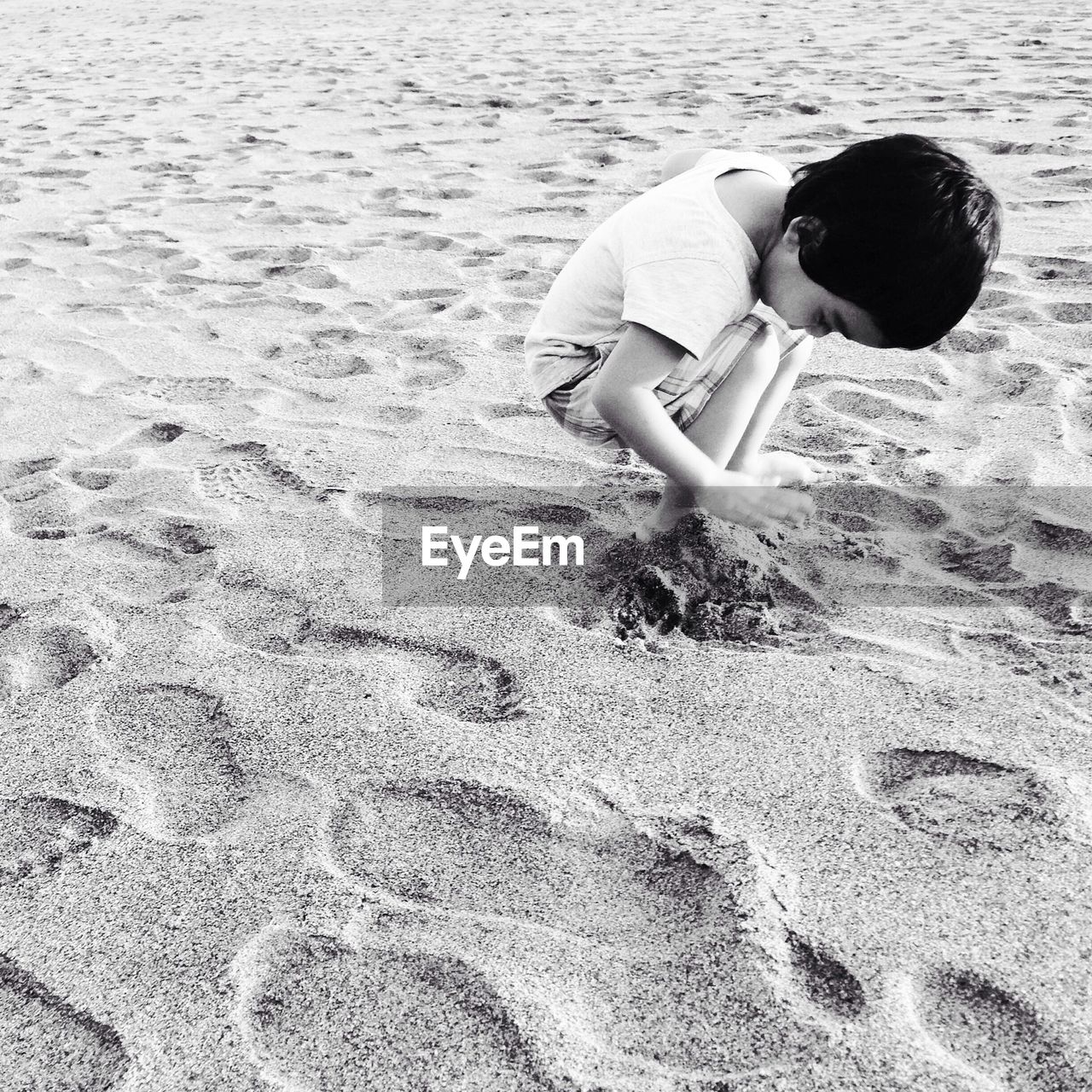 Cute boy playing with sand at shore of beach