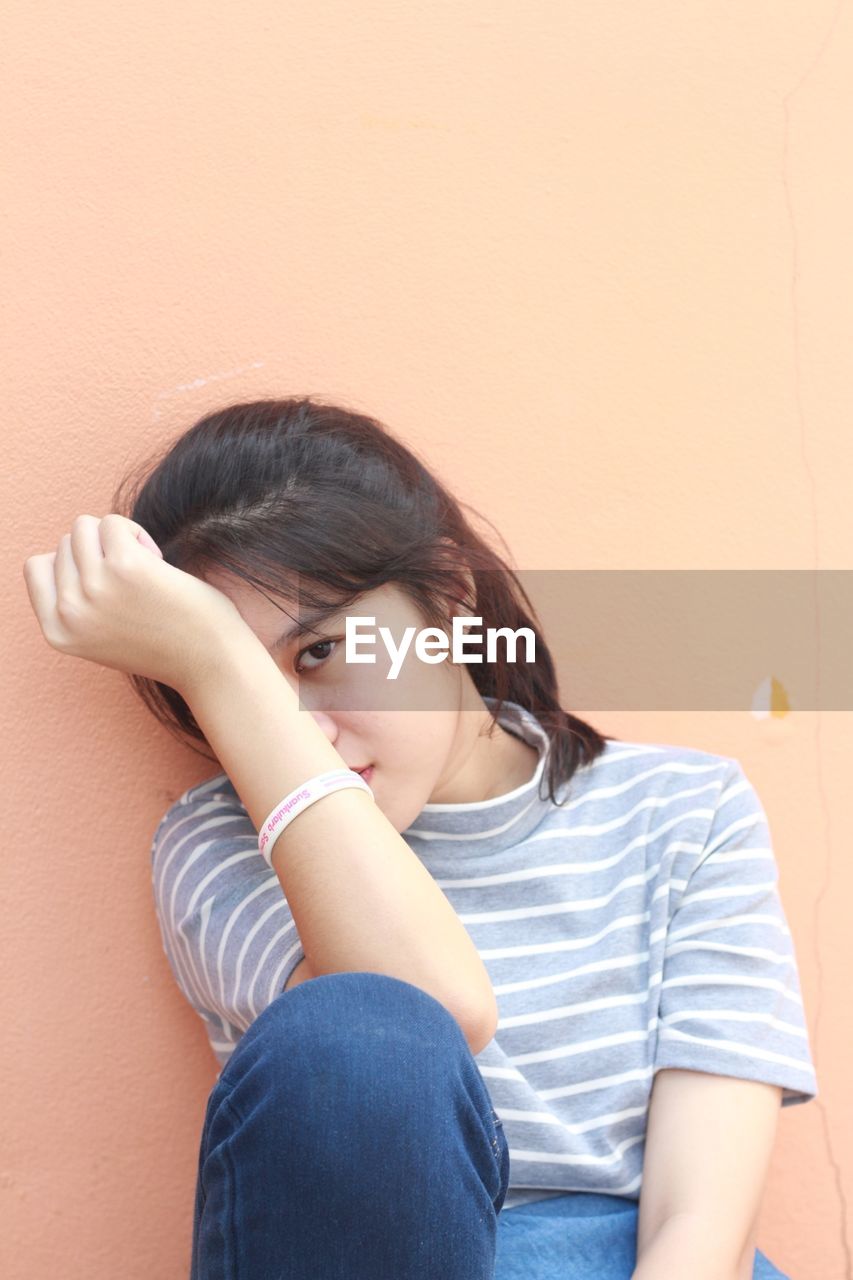 Close-up portrait of woman sitting against wall