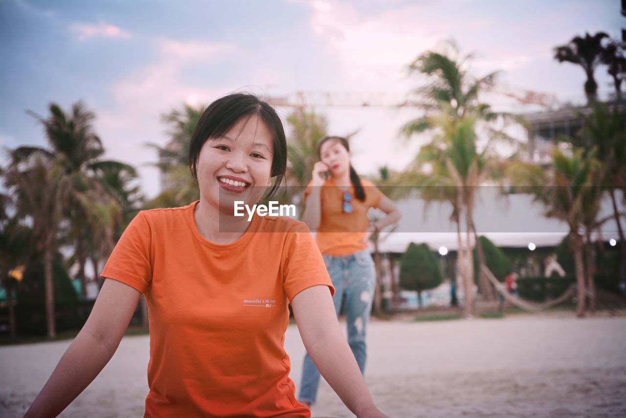 PORTRAIT OF SMILING WOMAN STANDING ON PALM TREE