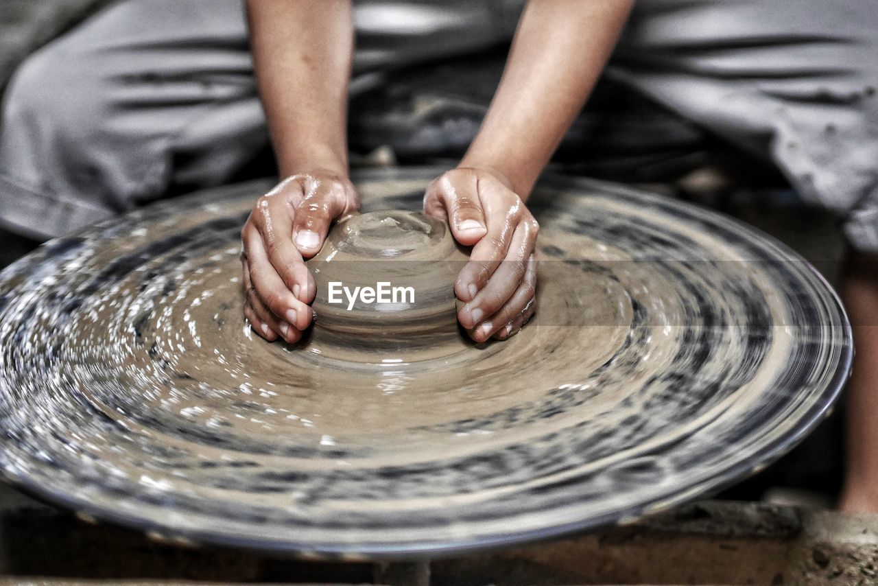 Cropped hands of potter making earthenware on pottery wheel