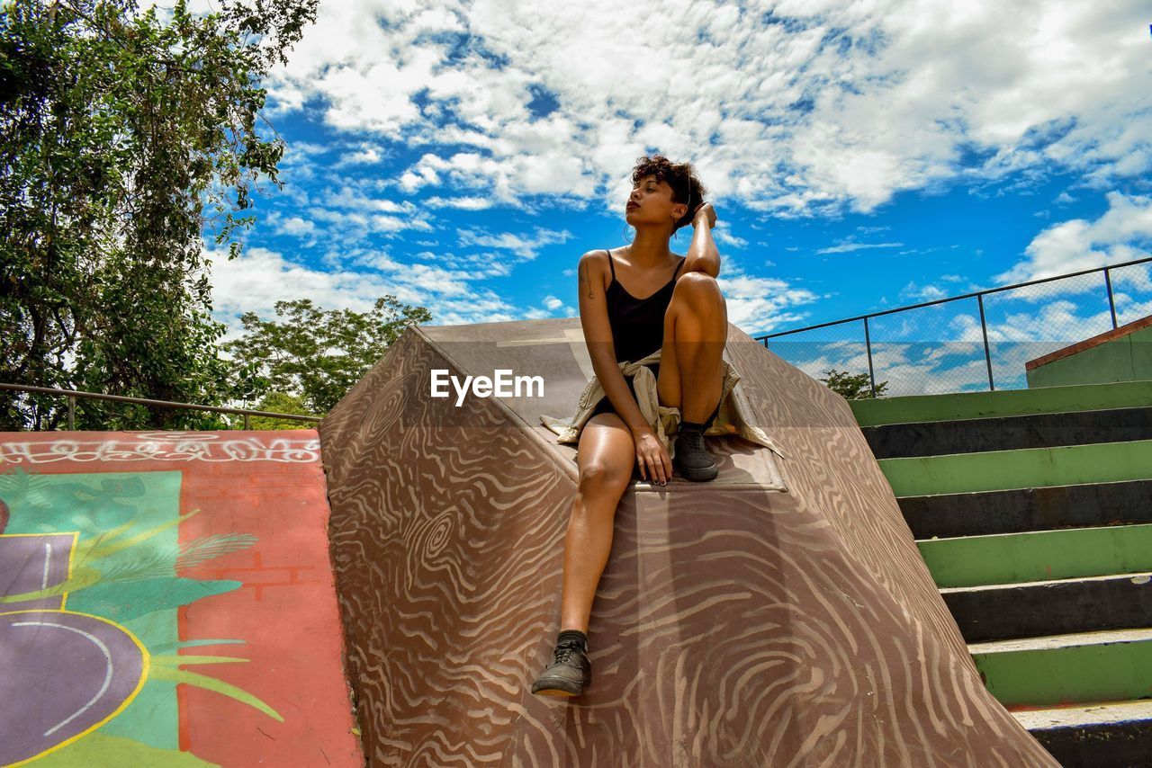 Woman looking away while sitting on railing against sky