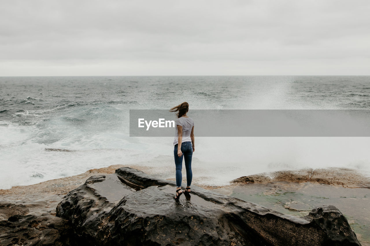 Rear view of woman standing on rock at beach