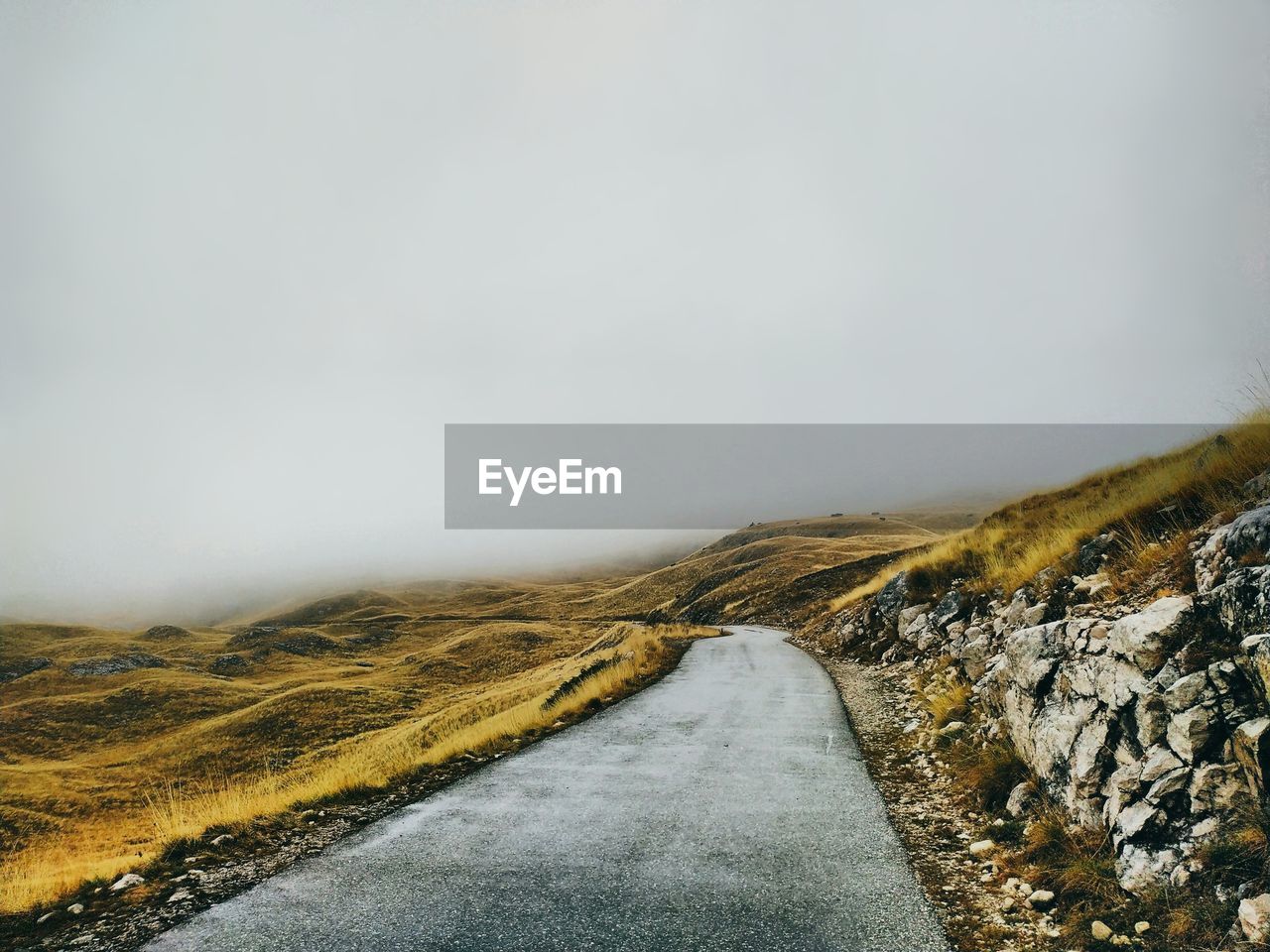 Road amidst landscape against sky during foggy weather