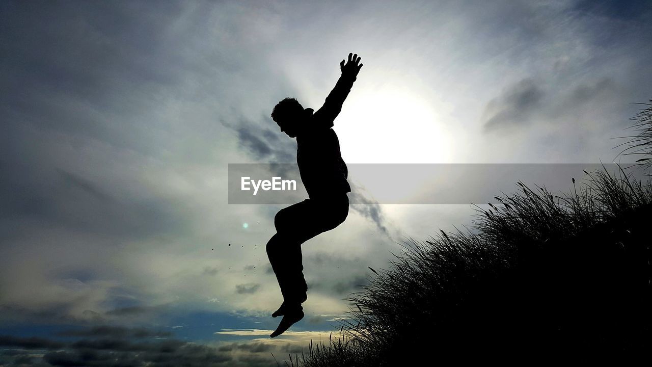 Low angle view of silhouette man jumping against sky