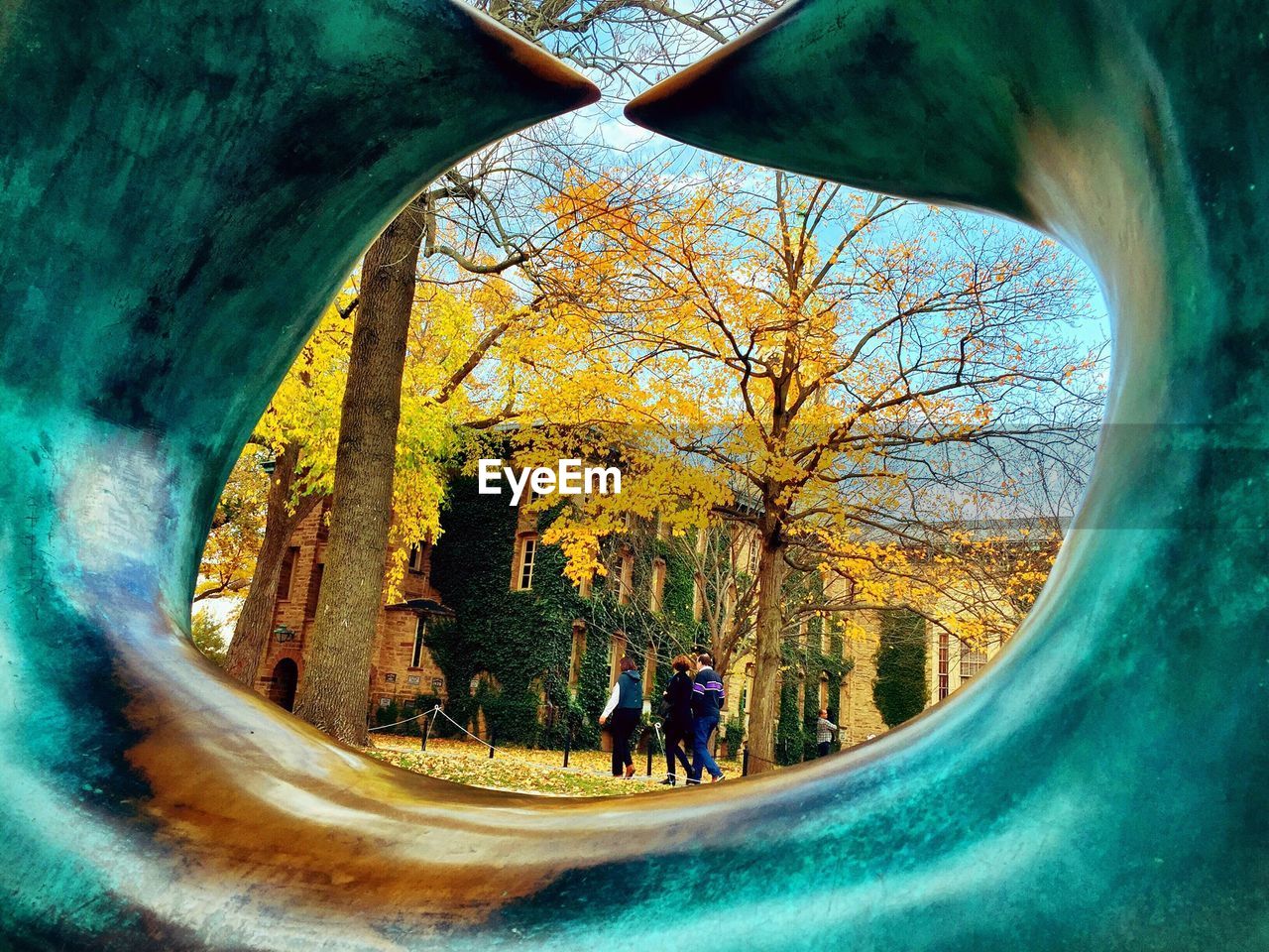 Rear view of people walking in park during autumn seen through curved metal