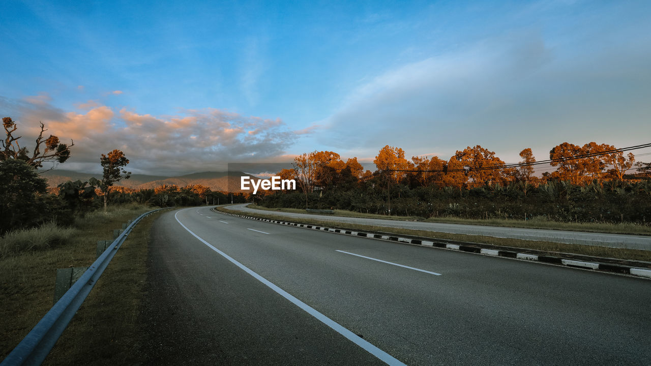 ROAD BY TREES AGAINST SKY DURING SUNRISE