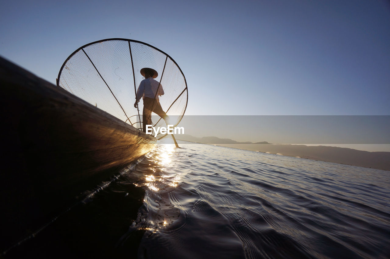 Rear view of fisherman with fishing net in boat on sea