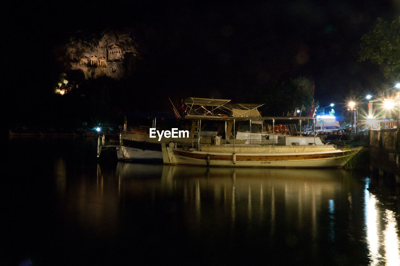 BOATS MOORED ON RIVER BY ILLUMINATED TREES AT NIGHT