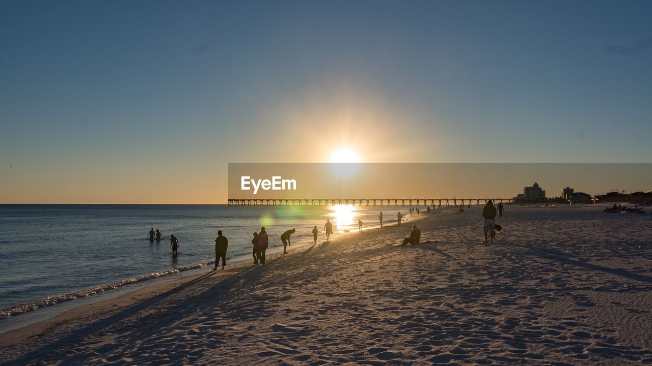 Silhouette people at beach against clear sky during sunset