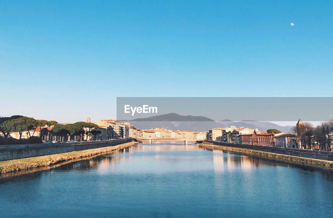 Scenic view of river by buildings against clear blue sky