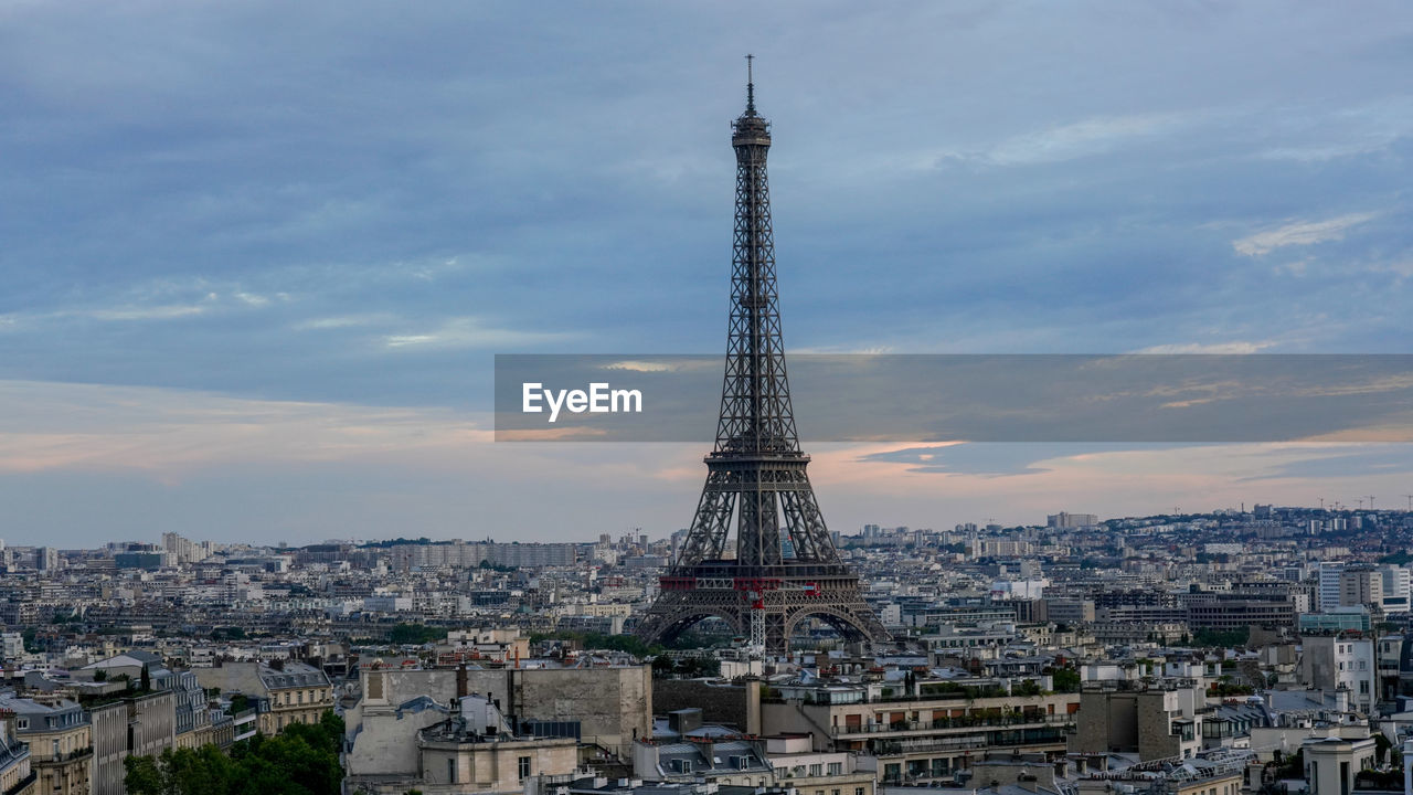 Eiffel tower amidst buildings in city against cloudy sky