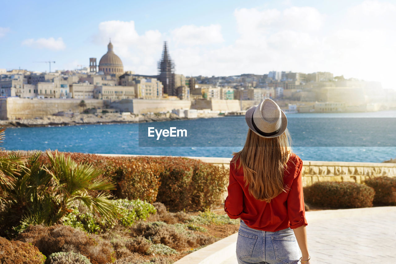 Woman with hat goes down along malta waterfront looking at beautiful cityscape of valletta, malta