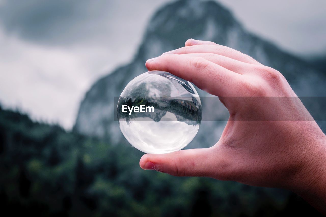 Cropped hand holding crystal ball against mountain