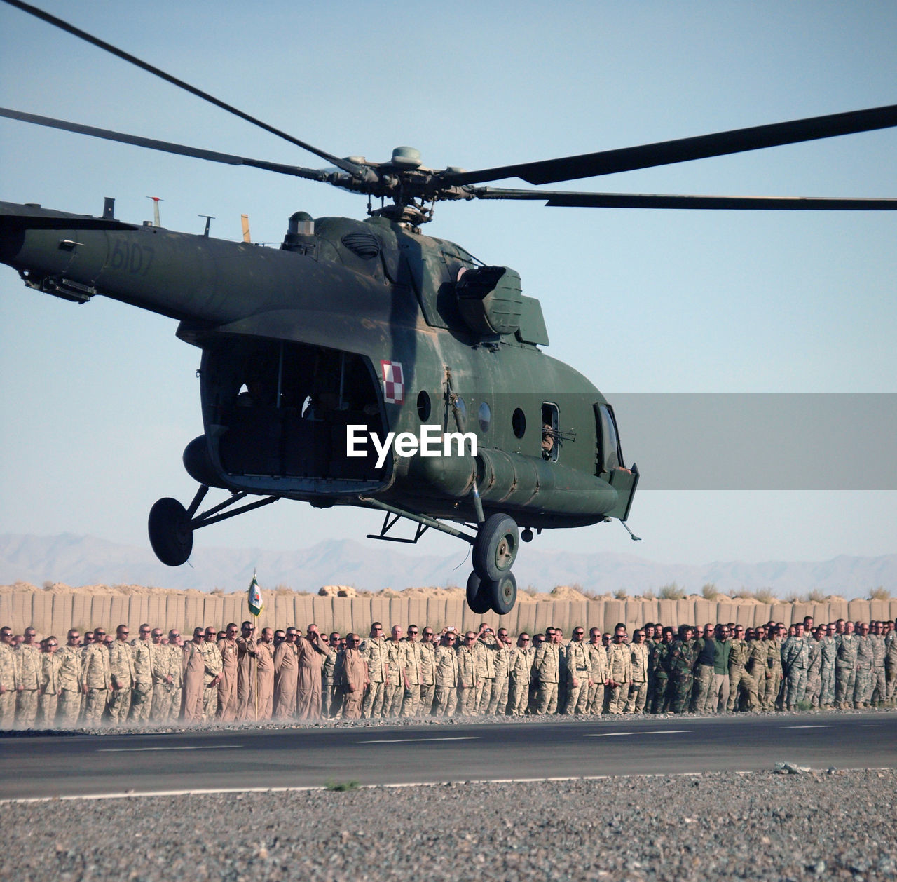 Helicopter flying against army soldiers standing on road