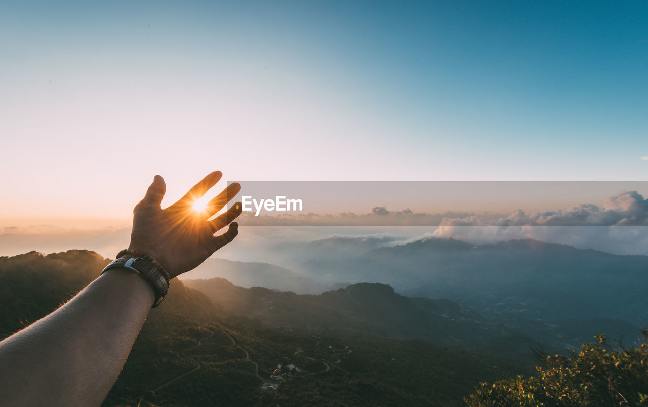 Copped hand of person against sky during sunset