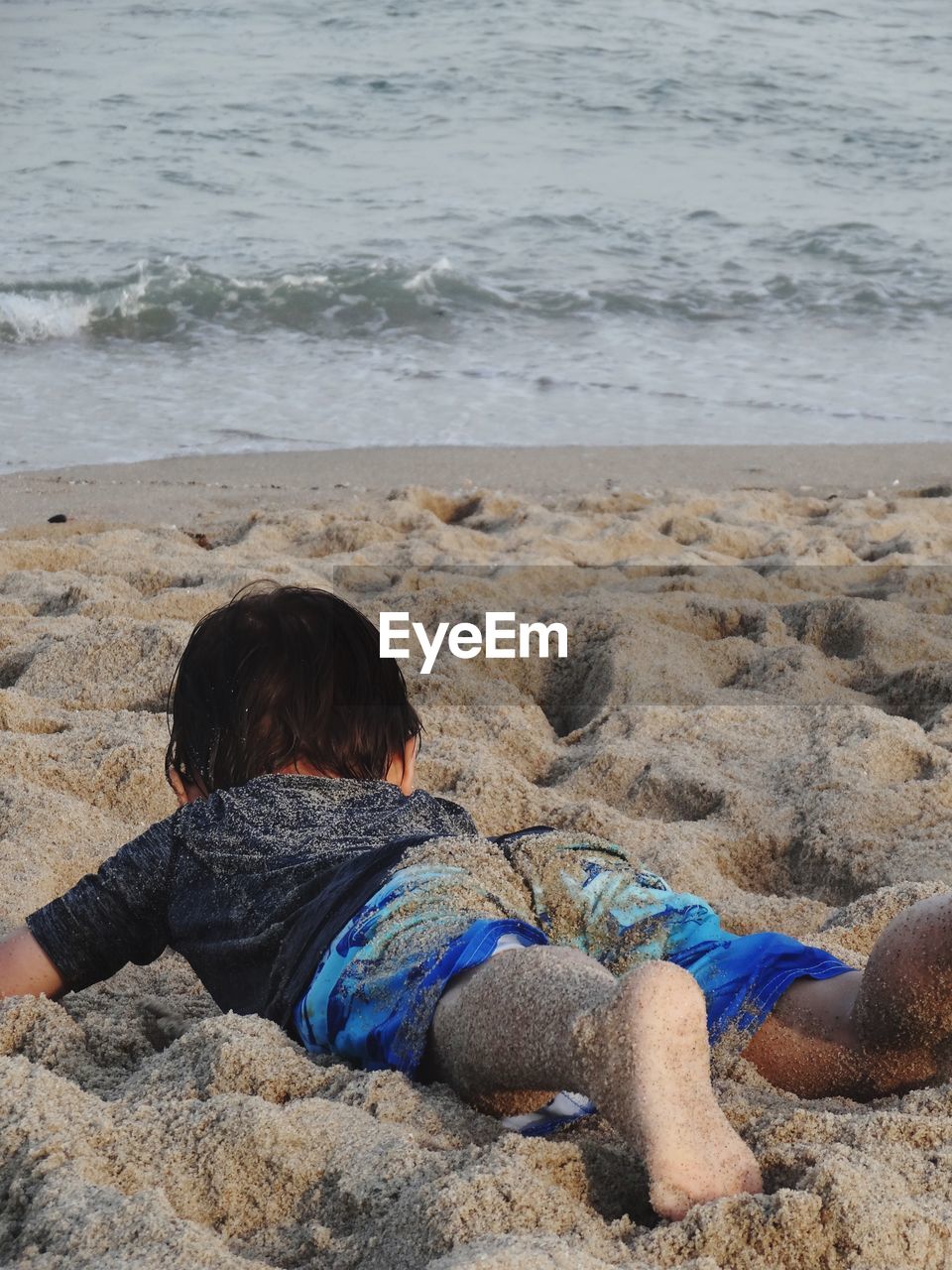 Full length of playful boy lying on sand at beach