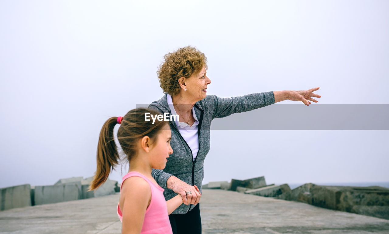 Grandmother and granddaughter standing on pier against sky