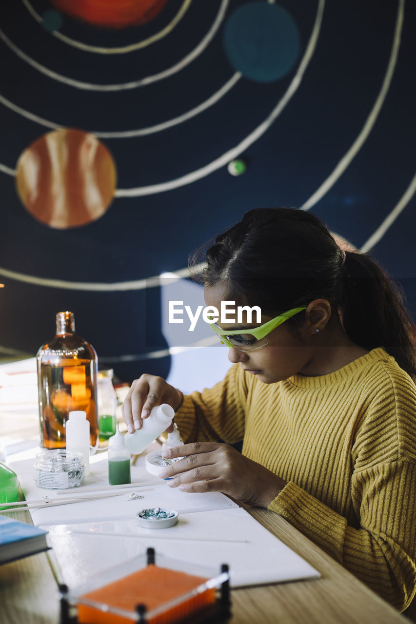 Motivated girl pouring chemical while doing scientific experiment at table