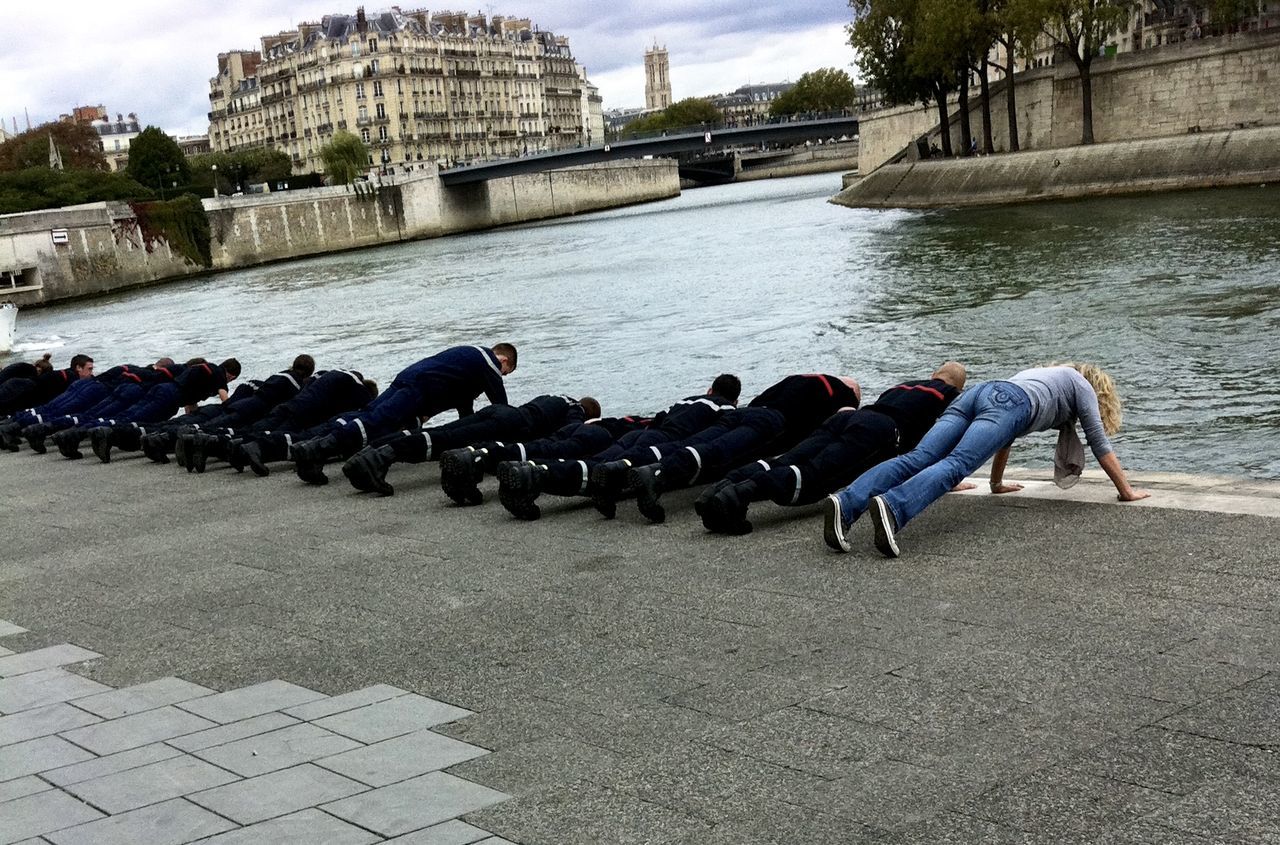 Woman with firefighters doing push-ups at promenade by seine river