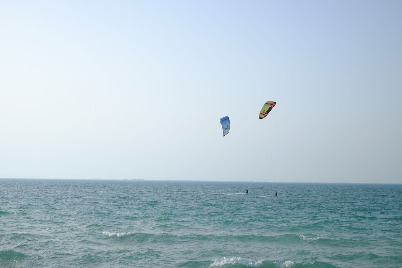 Person paragliding over sea against clear sky