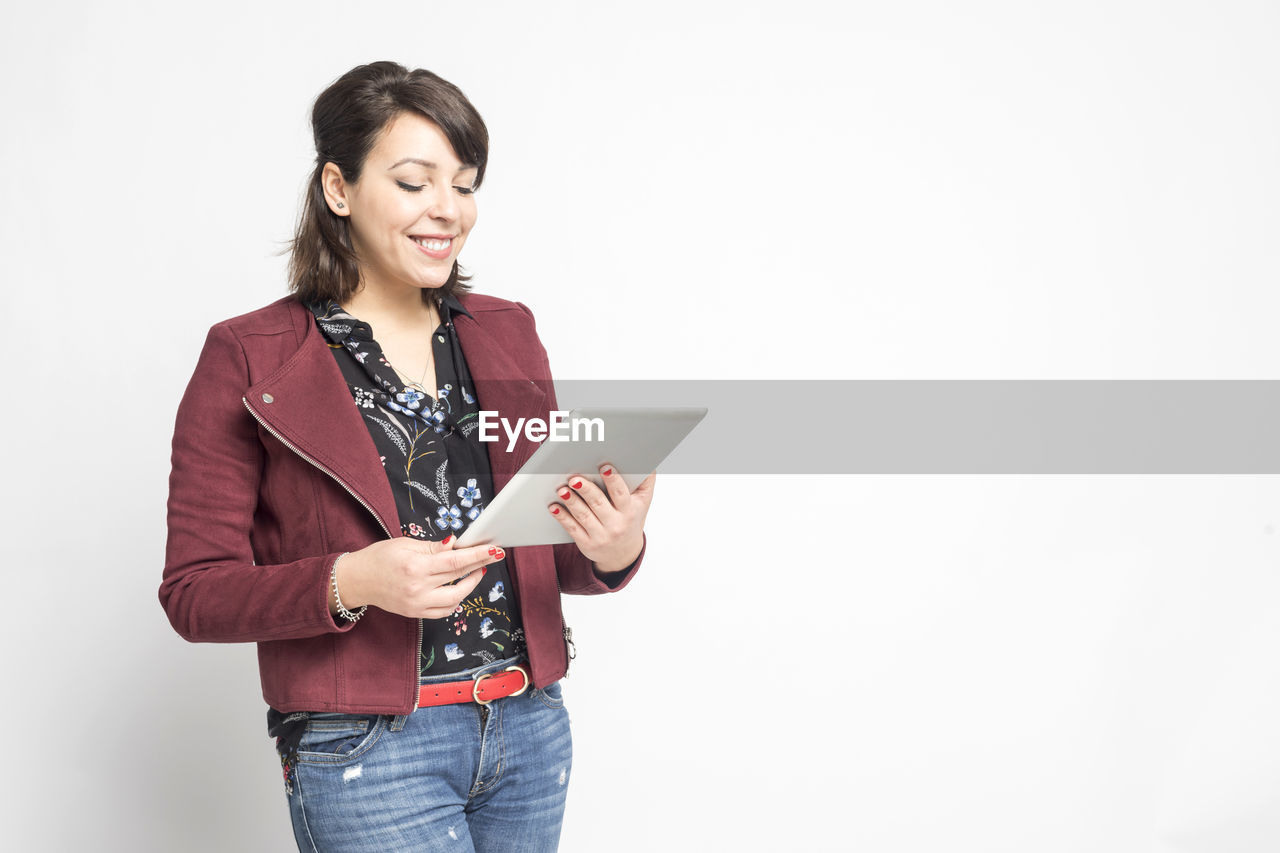 one person, adult, women, wireless technology, technology, indoors, copy space, communication, digital tablet, photo shoot, casual clothing, smiling, standing, young adult, computer, happiness, looking, holding, three quarter length, internet, studio shot, clothing, front view, business, white background, computer network, portrait, fashion, business finance and industry, jacket, emotion, hairstyle, cheerful, lifestyles, person, female, portable information device, portability, long hair, occupation, outerwear, laptop