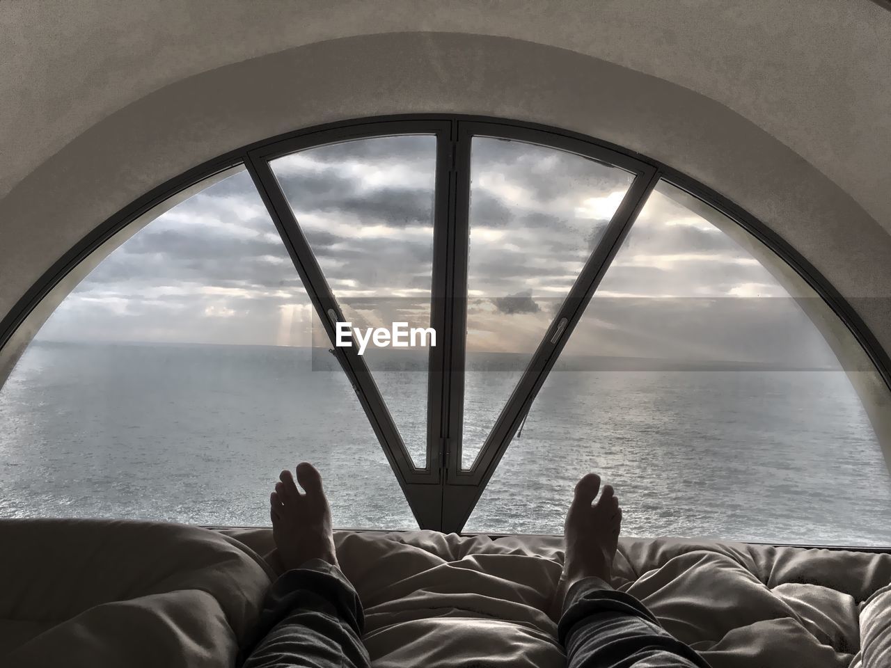 Low section of man lying on bed with sea seen through window