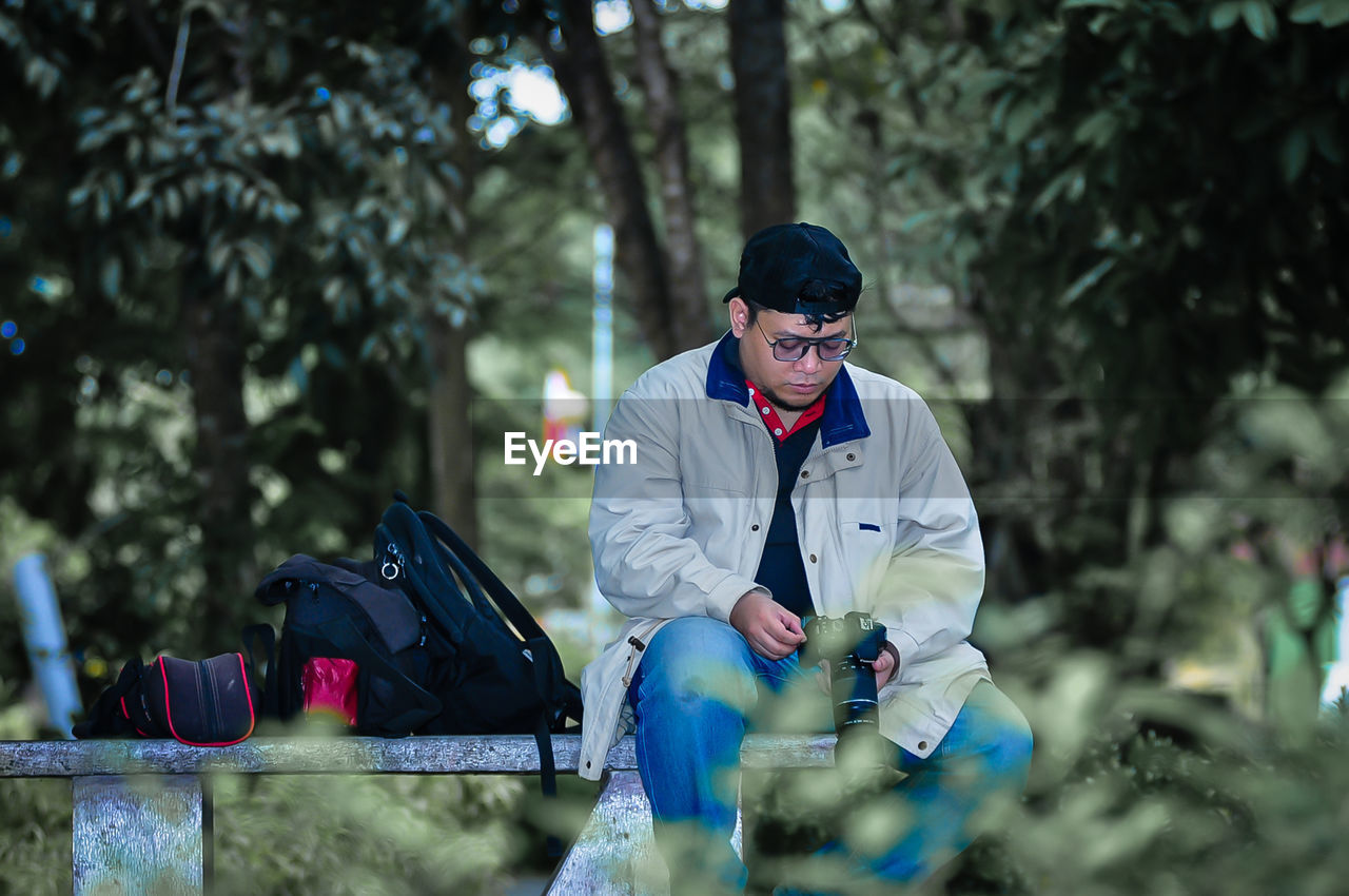 Side view of man using mobile phone while standing against trees