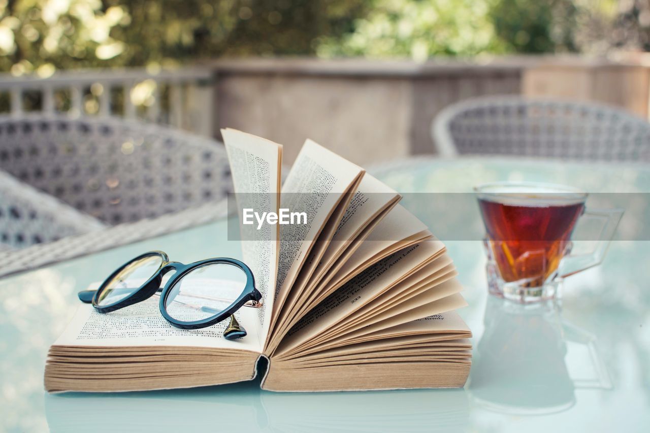Close-up of eyeglasses and book with drink on table
